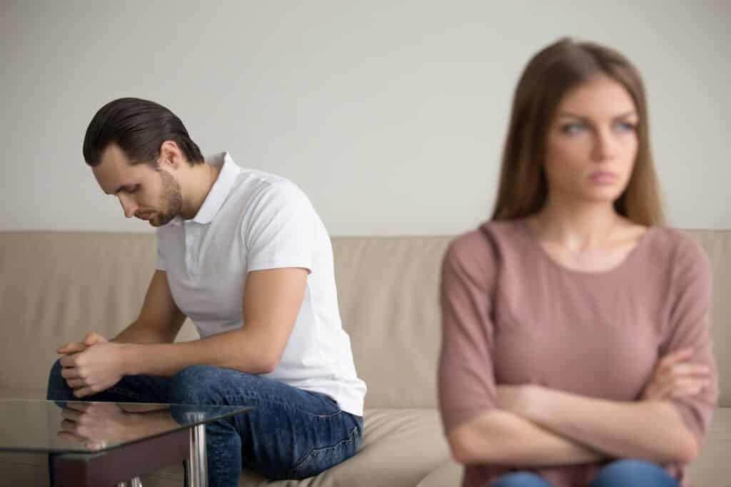 Upset depressed guy sitting on couch deep in thoughts, frustrated couple after quarrelling, guilty man regretting about mistake thinking of resolving conflict, offended woman not going to forgive