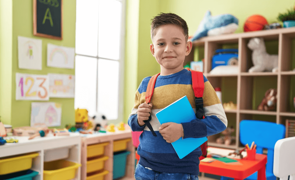 boy student wearing backpack holding book at kindergarten (1)