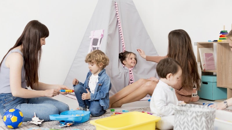 Two women playing with three children in a playroom