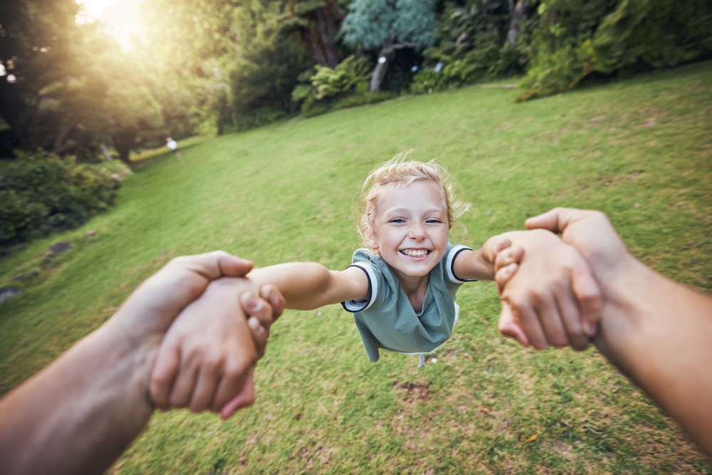 Child swinging from hands in park, pov and happy summer evening. Fun time, motion and girl in garde.