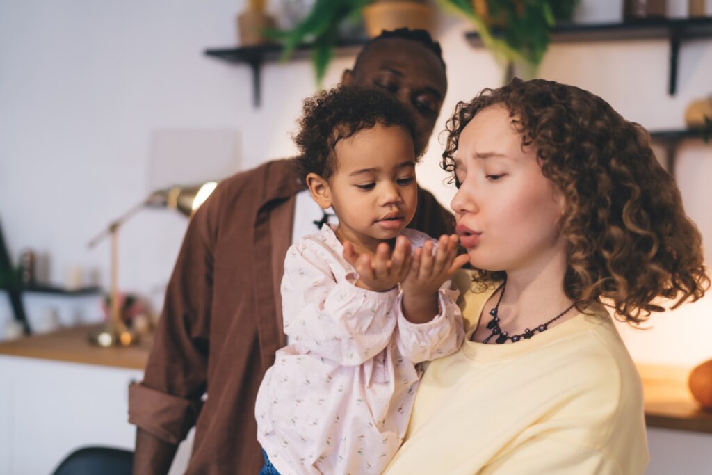 Cute child opening hands while carried by loving mother together with father in room