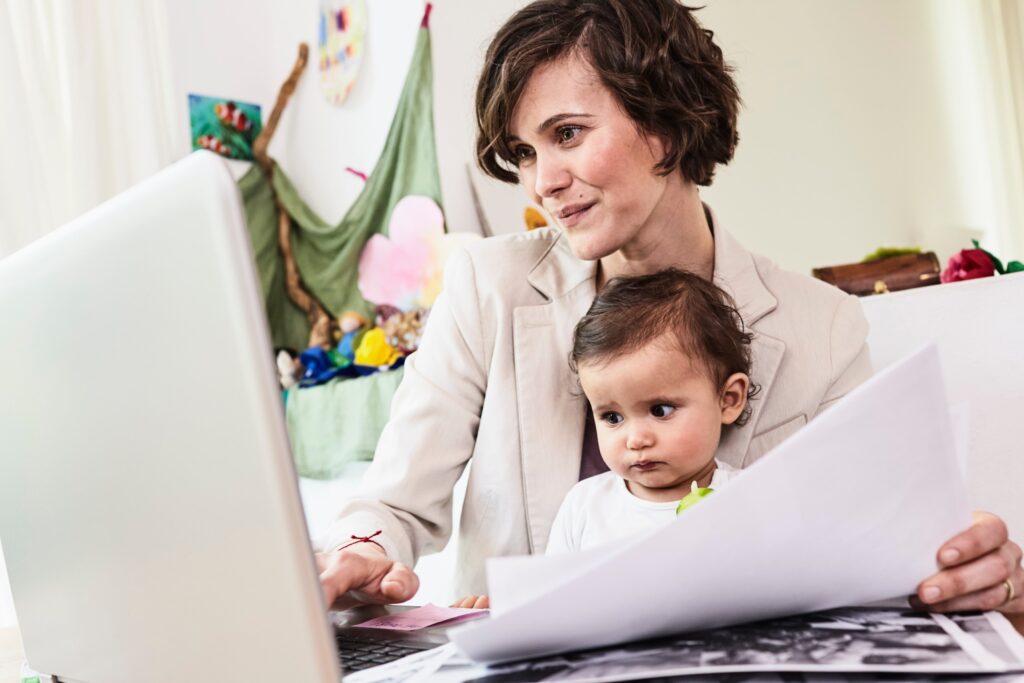 Mother holding sitting with baby daughter, working on laptop application for consent orders