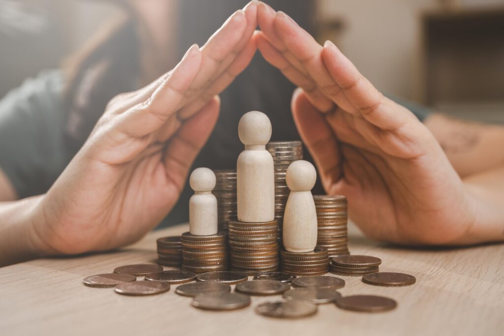 Family insurance plan protect. Help medicine protection. Father mother children insurance. A hand is protecting three small figurines and a pile of coins. Concept of financial security and protection.