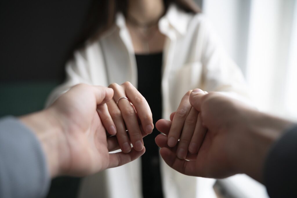 A waist up shot shows two people holding hands indoors.