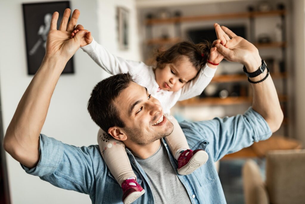 Carefree father carrying his small daughter on his shoulder at home.