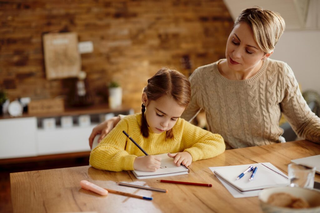 Small girl drawing on the paper while homeschooling with her mother.