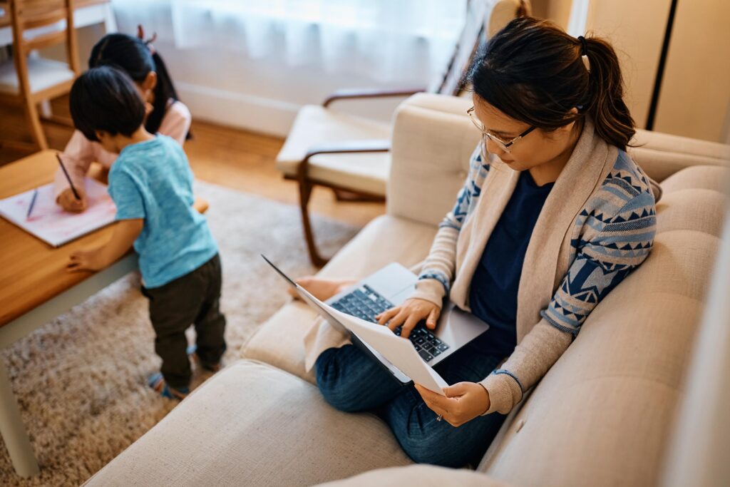 stay at home mother working on laptop while her kids are playing in the background.