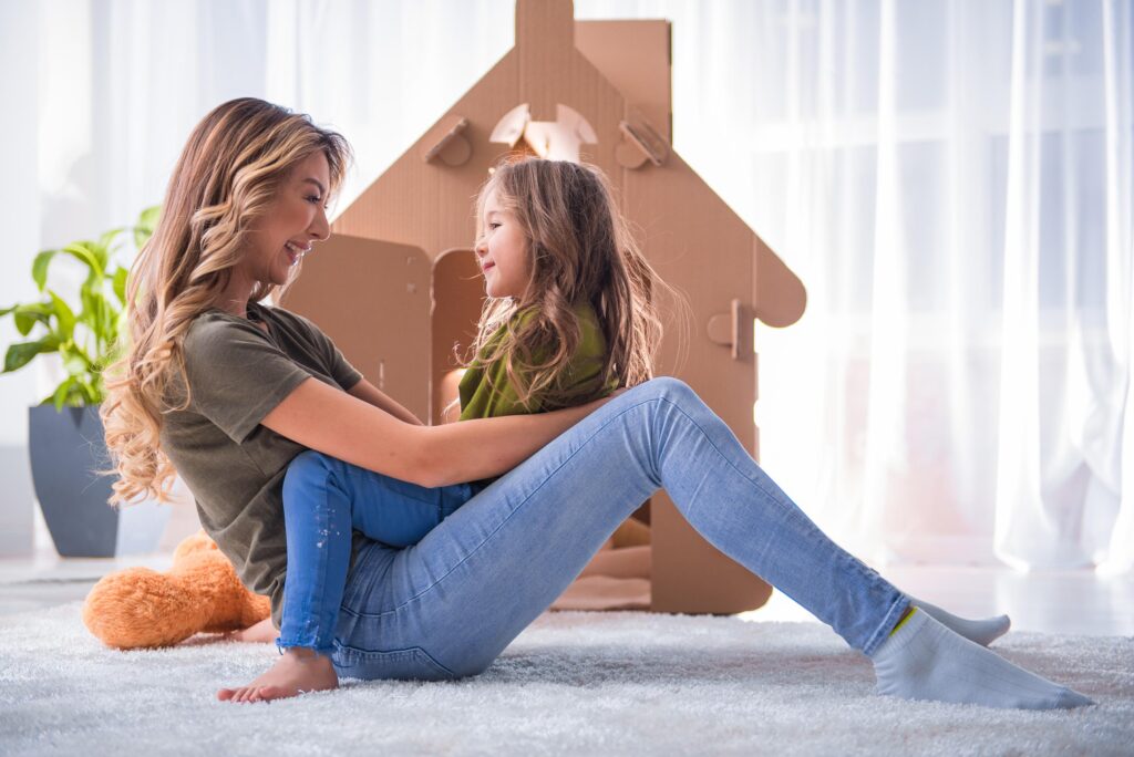 Mother and Daughter Playfully Interact by Cardboard House