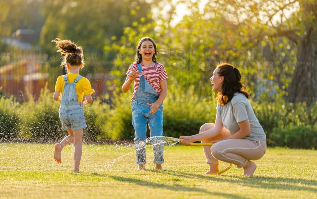 Children Playing with Water Hose on Lawn